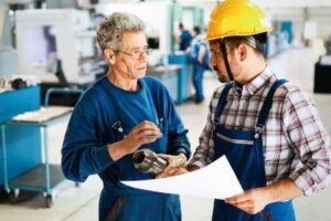 Two workers in a factory discussing a blueprint