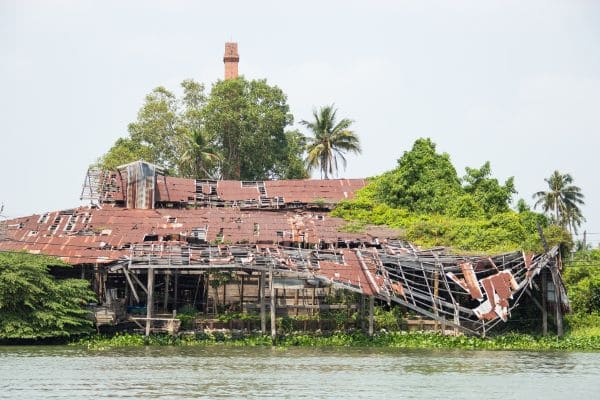 Dilapidated building surrounded by greenery and water.