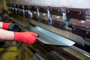 Worker bending sheet metal with press brake.