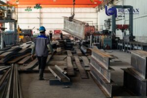 Worker guiding steel beam in factory