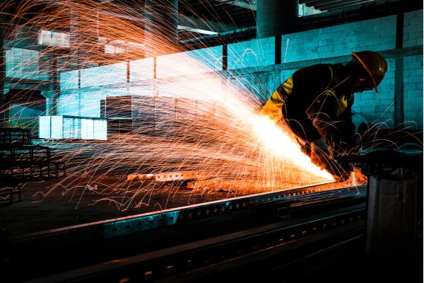 A worker uses a laser cutter to weld steel in a factory setting, focused on precision and safety.