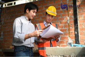 Two construction engineers reviewing building plans at a job site with safety gear