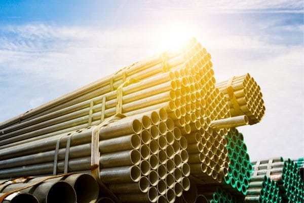 Bundles of galvanized steel pipes stacked in an industrial yard under sunlight.