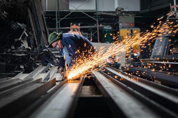 Skilled worker cutting structural steel beams with precision grinding during industrial steel fabrication process.